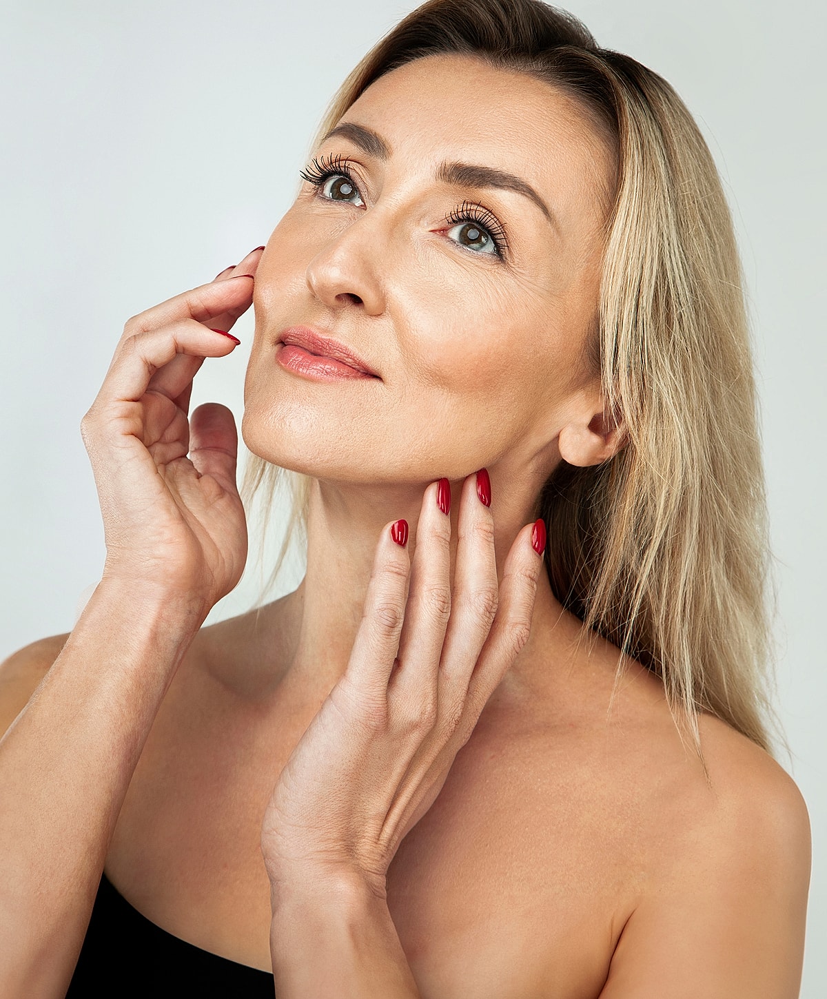 Tucson Blepharoplasty model touching her face with red nails.