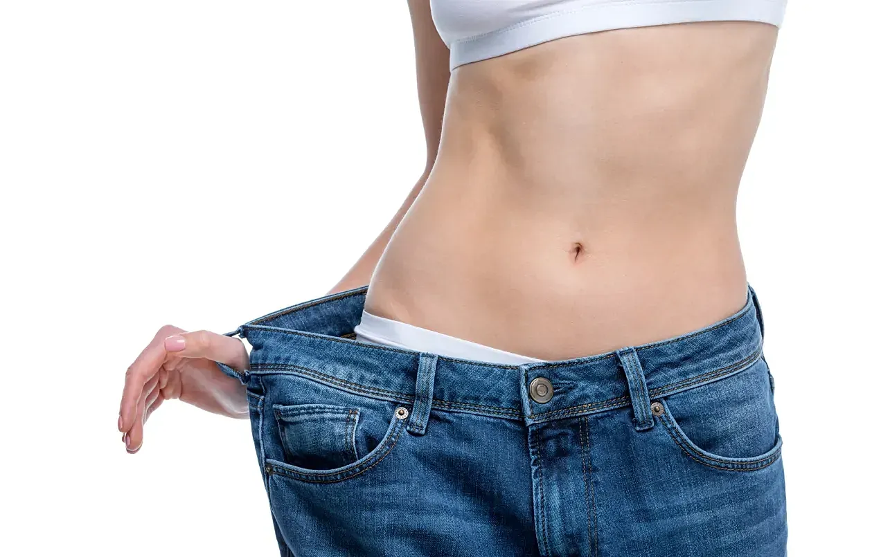 Tucson Liposuction model holding oversized jeans with a flat stomach.