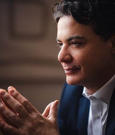 Man in suit contemplating thoughtfully with hands together.